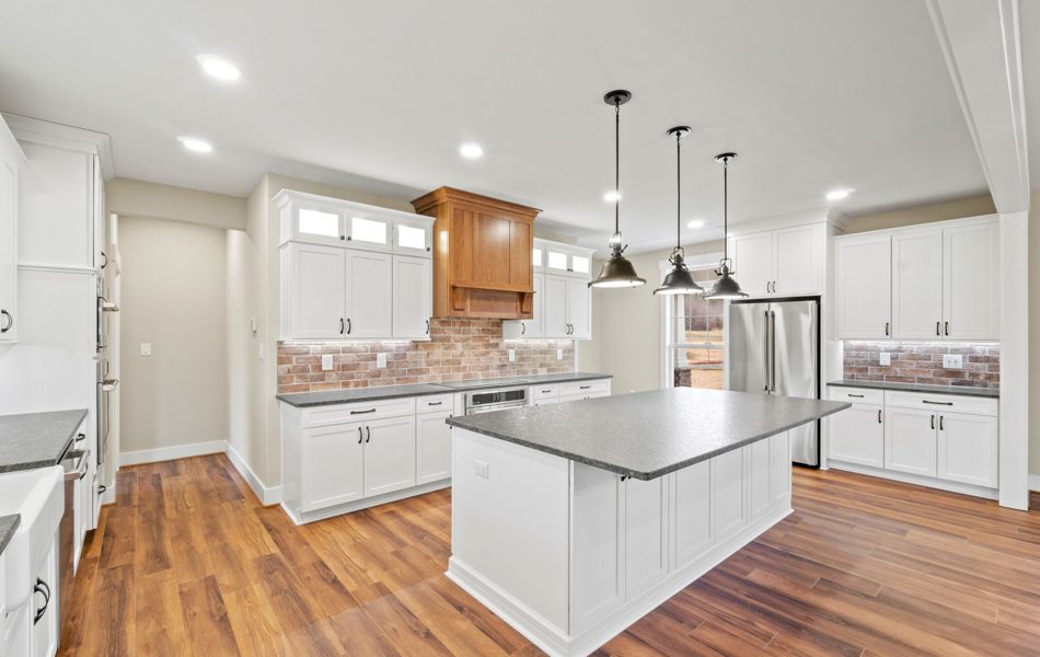 A remodeled kitchen with U-shaped design, and an island with hanging light fixtures, cabinets with recessed lights, a tile with brick-looking backsplash, and hardwood floors