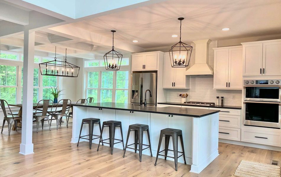 A kitchen and dining area remodeled, a kitchen island with stools, white cabinets, steel appliances, caged chandeliers, and hardwood flooring